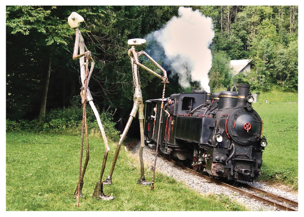 Eisenbahnerlebnis und Kunst im Bregenzerwald.
Die Heißdampflok Uh 102 (Bj. 1931) passiert mit einem Personenzug die „Eisenmänner auf Reisen“.